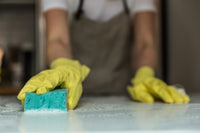 person cleaning a counter top in gloves with a green sponge